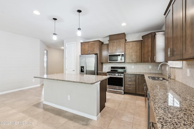 kitchen with sink, light stone counters, decorative light fixtures, a center island, and stainless steel appliances