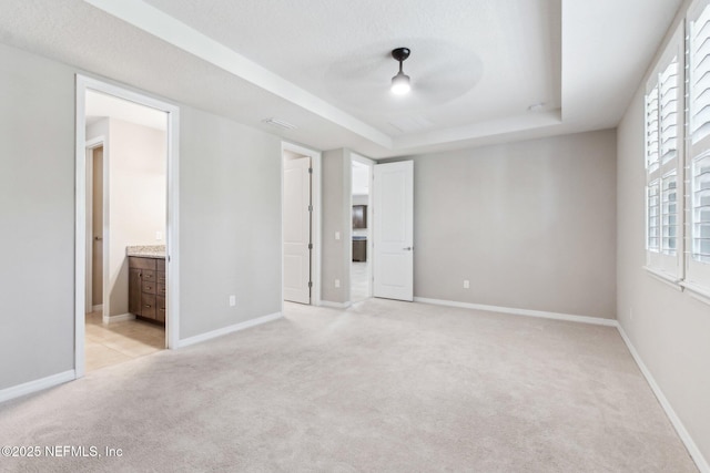 unfurnished bedroom featuring connected bathroom, light carpet, and a tray ceiling