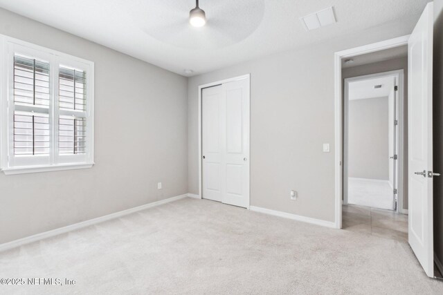 unfurnished bedroom with light colored carpet, a closet, and ceiling fan