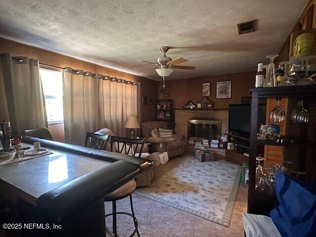 living room featuring light colored carpet, a textured ceiling, ceiling fan, and wood walls