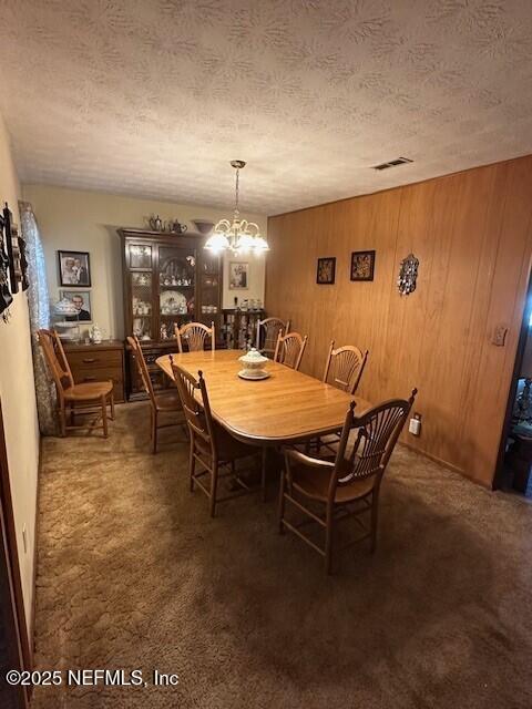 dining area with dark colored carpet, wooden walls, a textured ceiling, and a notable chandelier