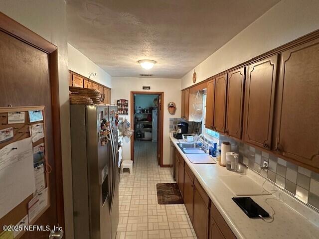 kitchen with sink, stainless steel fridge, a textured ceiling, and decorative backsplash