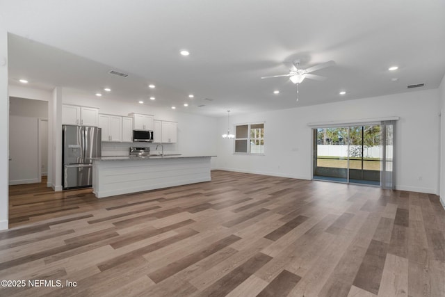 unfurnished living room with sink, ceiling fan with notable chandelier, and light hardwood / wood-style flooring