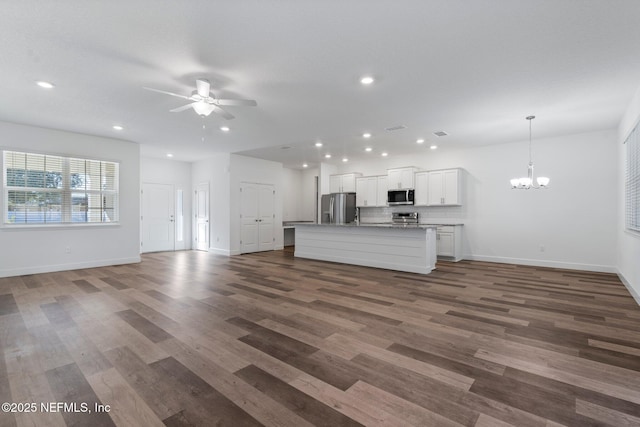 unfurnished living room with ceiling fan with notable chandelier and dark hardwood / wood-style floors