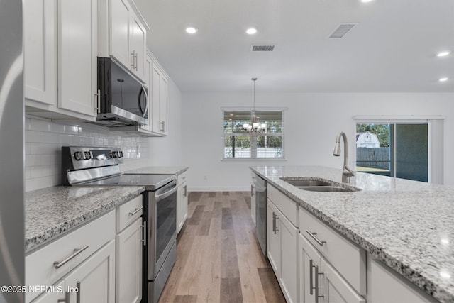 kitchen featuring pendant lighting, white cabinetry, sink, stainless steel appliances, and light stone countertops