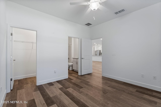 unfurnished bedroom with dark wood-type flooring, connected bathroom, a walk in closet, stainless steel fridge, and a closet