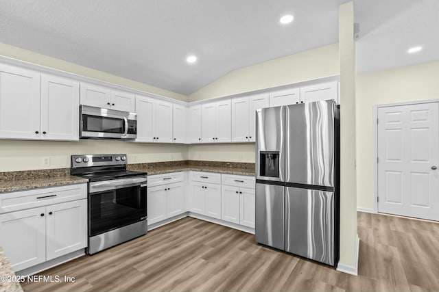 kitchen featuring lofted ceiling, white cabinetry, light hardwood / wood-style flooring, dark stone countertops, and stainless steel appliances