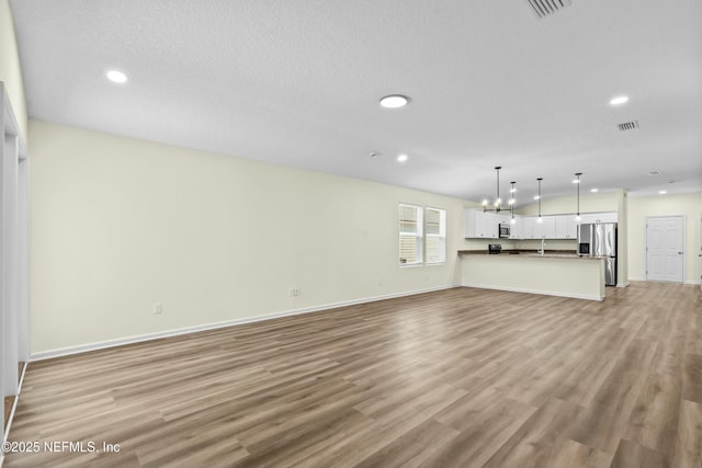 unfurnished living room with a chandelier, a textured ceiling, and light wood-type flooring