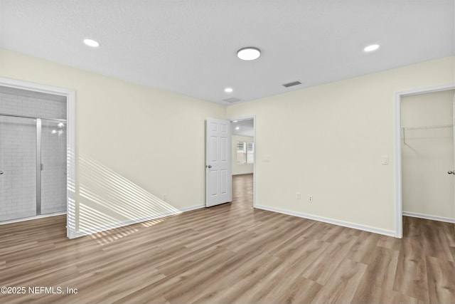 unfurnished bedroom with a spacious closet, a textured ceiling, light hardwood / wood-style floors, and a closet