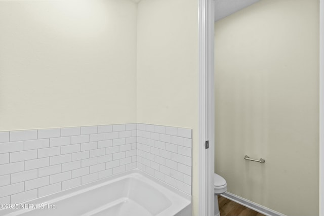 bathroom featuring hardwood / wood-style flooring, a bath, and toilet