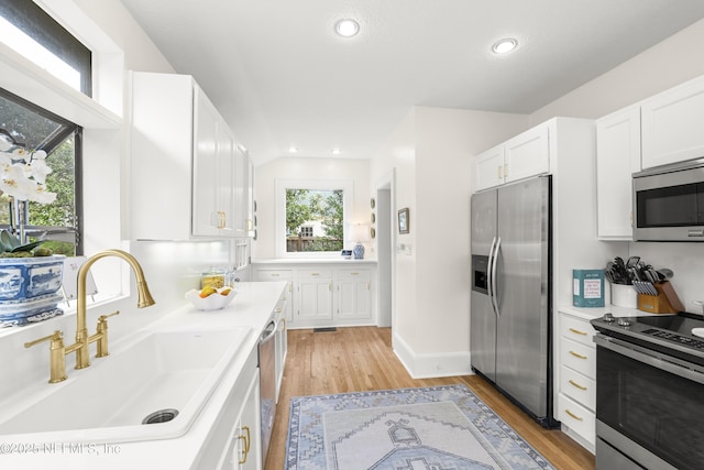 kitchen featuring vaulted ceiling, white cabinetry, sink, stainless steel appliances, and light hardwood / wood-style flooring