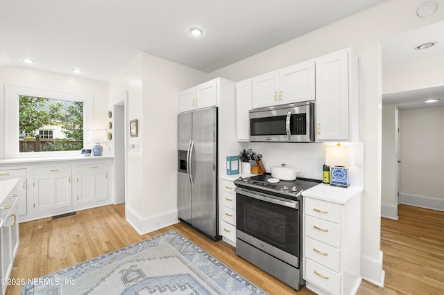 kitchen with appliances with stainless steel finishes, light hardwood / wood-style floors, and white cabinets