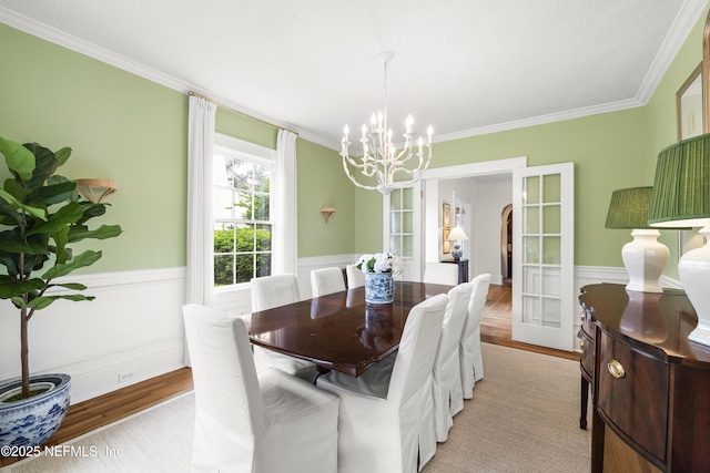 dining space with crown molding, light wood-type flooring, an inviting chandelier, and french doors