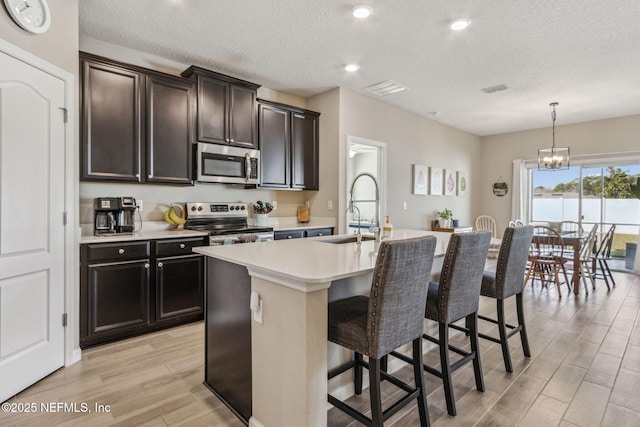 kitchen featuring an island with sink, appliances with stainless steel finishes, a kitchen breakfast bar, wood finish floors, and a sink