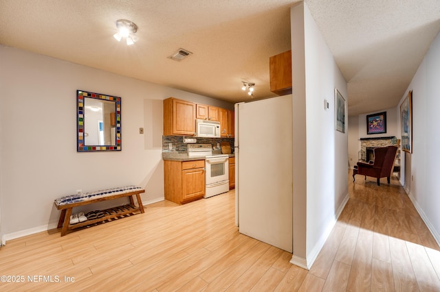 kitchen featuring white appliances, a textured ceiling, decorative backsplash, and light wood-type flooring