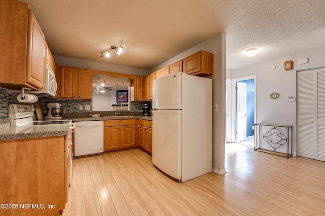 kitchen with sink, white appliances, backsplash, light hardwood / wood-style floors, and a textured ceiling