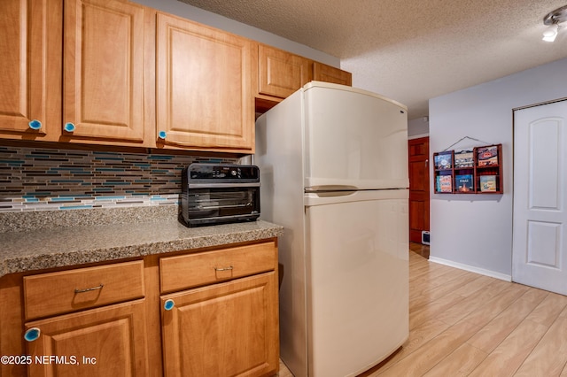 kitchen with white fridge, a textured ceiling, light hardwood / wood-style floors, and decorative backsplash