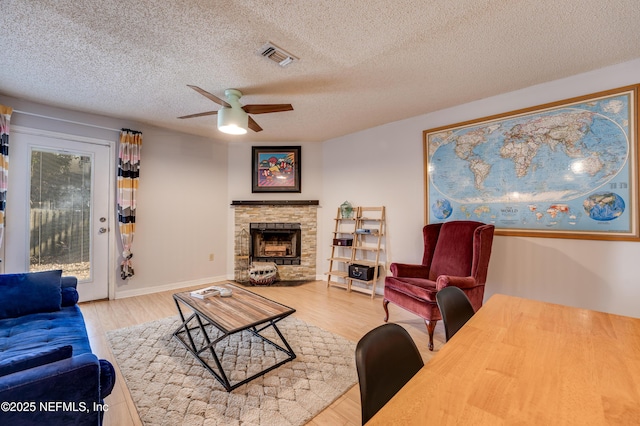 living room featuring ceiling fan, a textured ceiling, a fireplace, and light hardwood / wood-style flooring