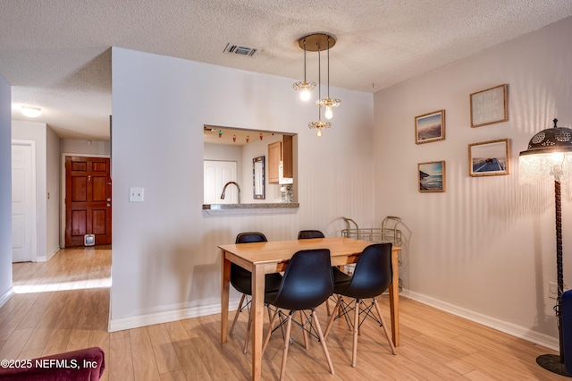 dining space featuring an inviting chandelier, a textured ceiling, and light hardwood / wood-style floors