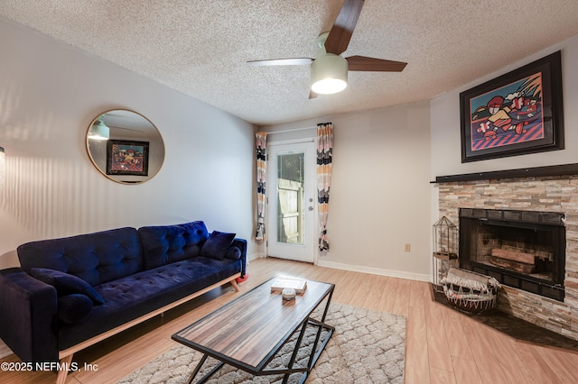 living room with hardwood / wood-style flooring, ceiling fan, a stone fireplace, and a textured ceiling