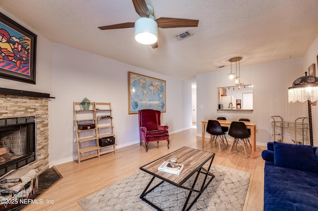 living room featuring a stone fireplace, light hardwood / wood-style floors, and a textured ceiling