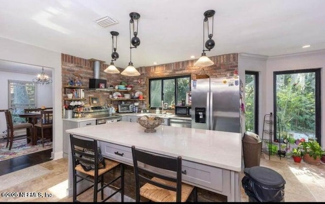 kitchen featuring gray cabinetry, a kitchen breakfast bar, a kitchen island, pendant lighting, and stainless steel appliances