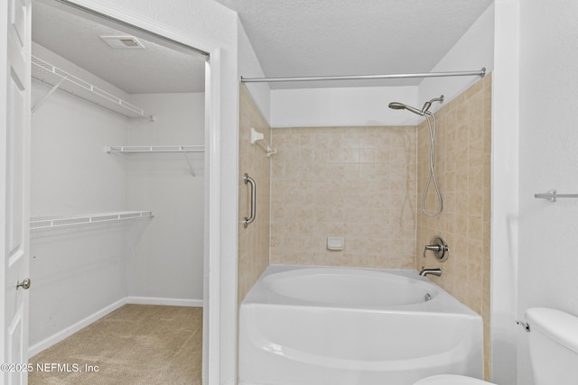 bathroom featuring tiled shower / bath, a textured ceiling, and toilet