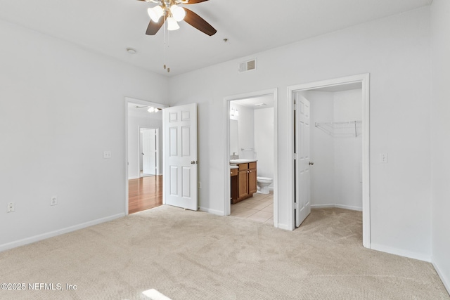 unfurnished bedroom with ceiling fan, connected bathroom, a spacious closet, light colored carpet, and a closet