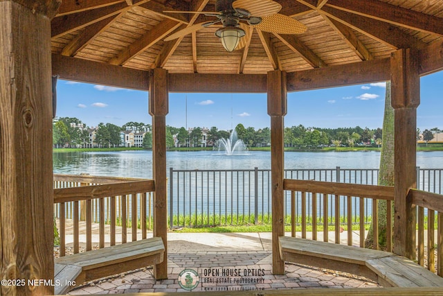 wooden terrace with a water view, ceiling fan, and a gazebo