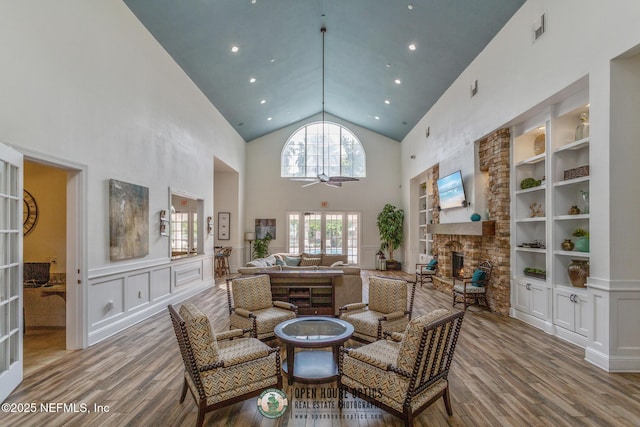 sitting room featuring light hardwood / wood-style flooring, ceiling fan, high vaulted ceiling, a fireplace, and built in shelves