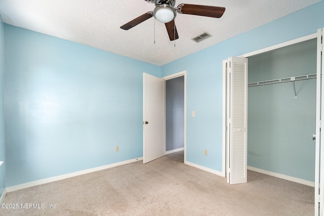 unfurnished bedroom featuring ceiling fan, light colored carpet, a textured ceiling, and a closet