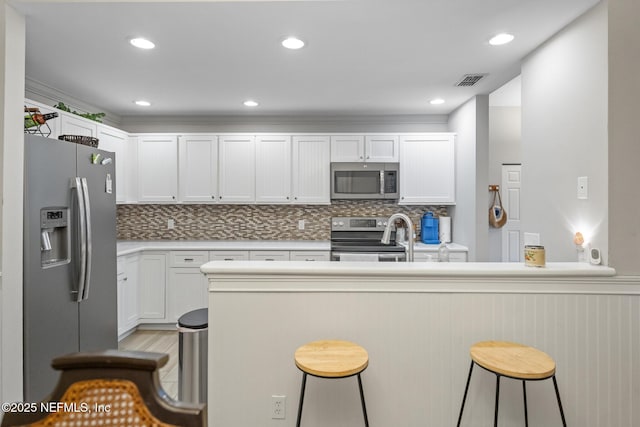 kitchen with white cabinetry, a breakfast bar, kitchen peninsula, and appliances with stainless steel finishes