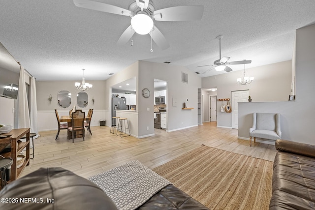 living room with lofted ceiling, ceiling fan with notable chandelier, a textured ceiling, and light wood-type flooring