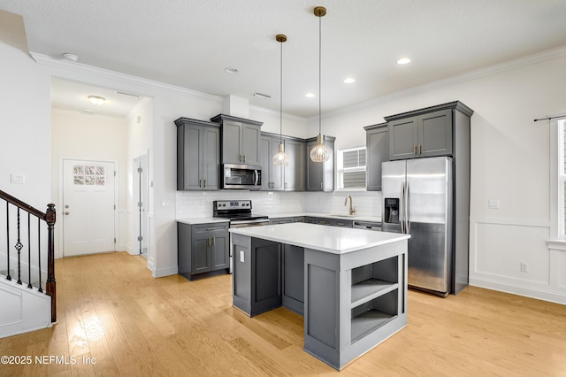 kitchen featuring gray cabinets, a kitchen island, appliances with stainless steel finishes, hanging light fixtures, and light hardwood / wood-style floors