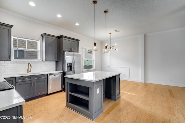 kitchen with a kitchen island, appliances with stainless steel finishes, pendant lighting, sink, and light wood-type flooring