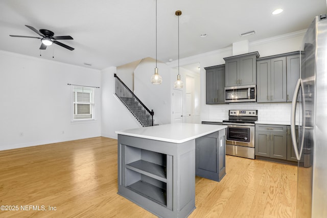 kitchen with gray cabinetry, hanging light fixtures, light wood-type flooring, a kitchen island, and stainless steel appliances