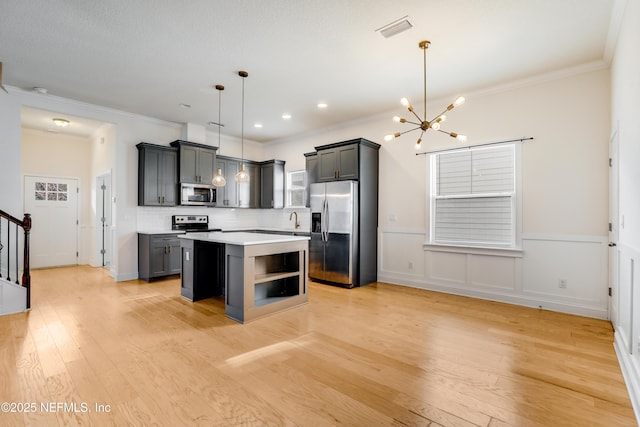 kitchen featuring pendant lighting, sink, appliances with stainless steel finishes, a kitchen island, and light wood-type flooring