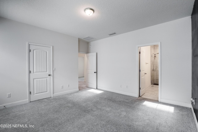 unfurnished bedroom with ensuite bath, light carpet, and a textured ceiling