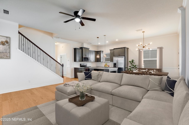 living room with ceiling fan with notable chandelier, light hardwood / wood-style flooring, and ornamental molding