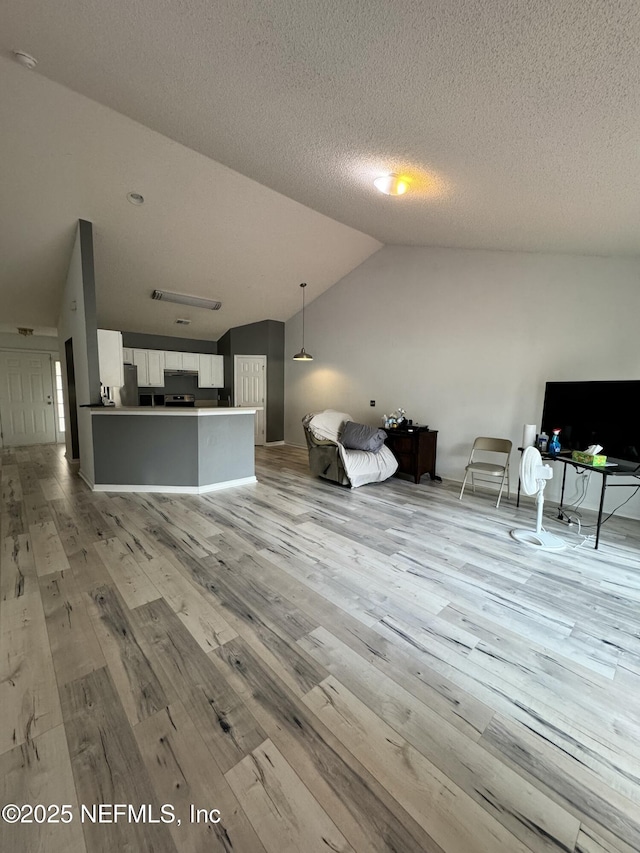 unfurnished living room with vaulted ceiling, a textured ceiling, and light wood-type flooring