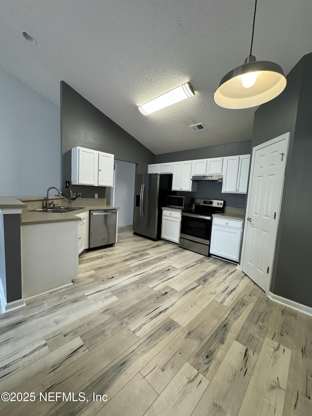 kitchen with lofted ceiling, sink, decorative light fixtures, appliances with stainless steel finishes, and white cabinets