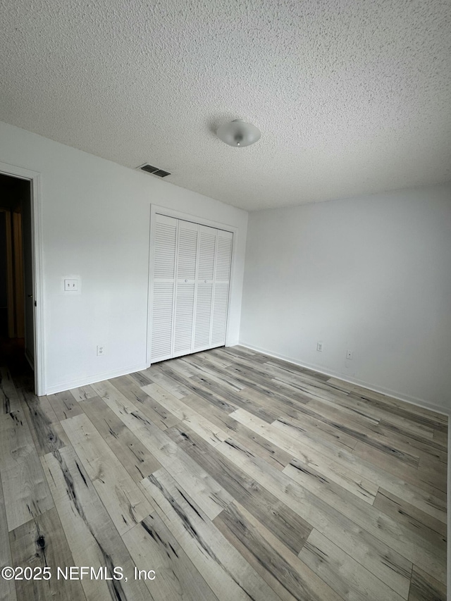 unfurnished bedroom featuring a closet, a textured ceiling, and light wood-type flooring