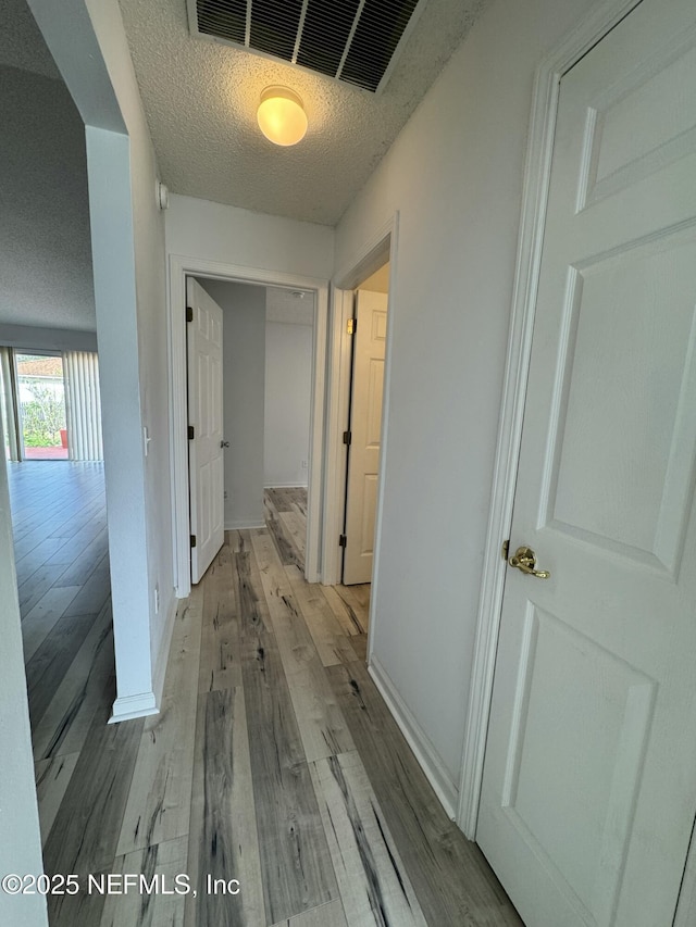 hall with a textured ceiling and light wood-type flooring