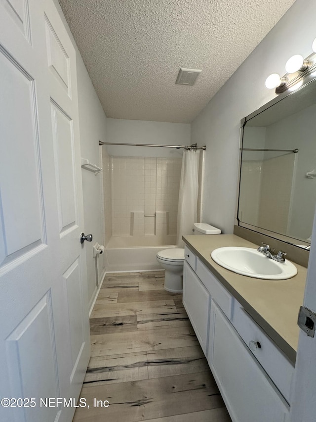 full bathroom with shower / bathtub combination with curtain, hardwood / wood-style flooring, vanity, a textured ceiling, and toilet