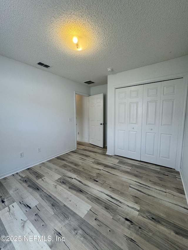 unfurnished bedroom with light hardwood / wood-style floors, a closet, and a textured ceiling