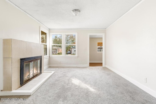 unfurnished living room featuring light colored carpet, ornamental molding, a tiled fireplace, and a textured ceiling