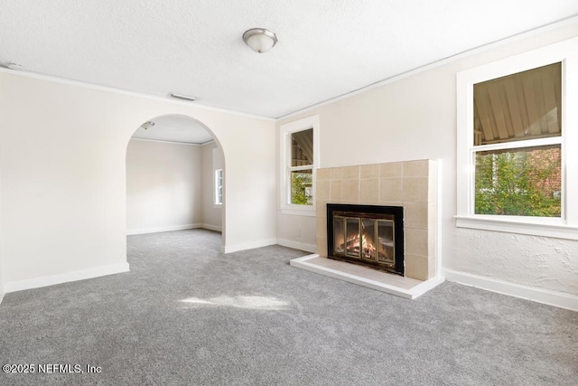 unfurnished living room featuring a tile fireplace, ornamental molding, carpet flooring, and a textured ceiling