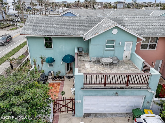 rear view of property featuring a balcony, a garage, and a patio