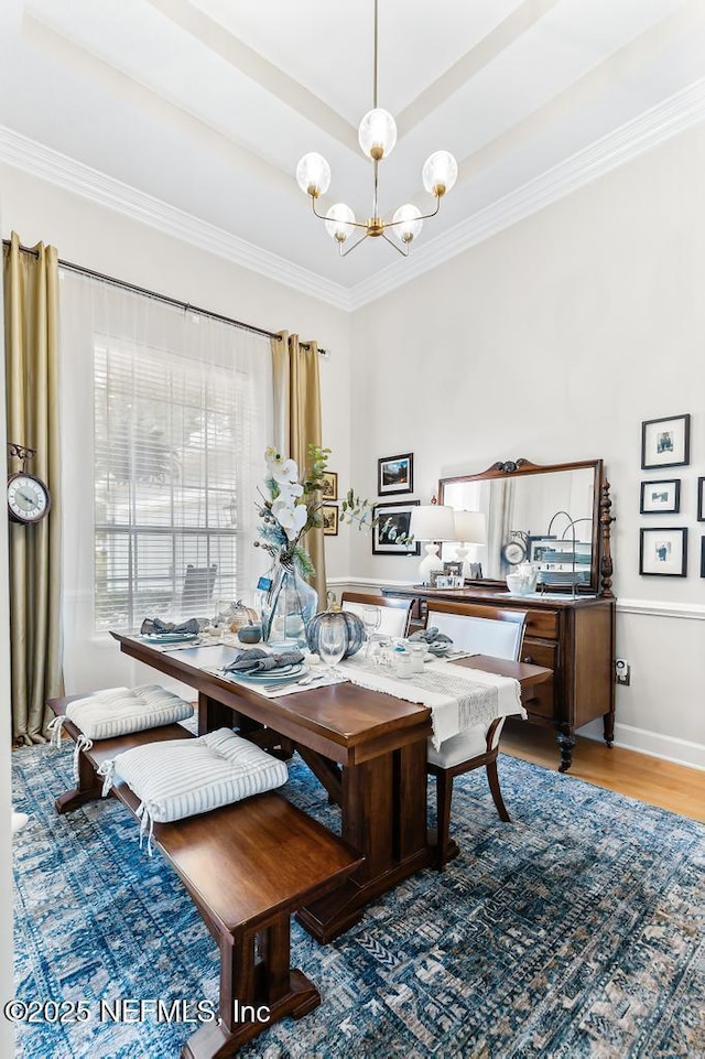 dining area with a raised ceiling, ornamental molding, light wood-type flooring, and an inviting chandelier