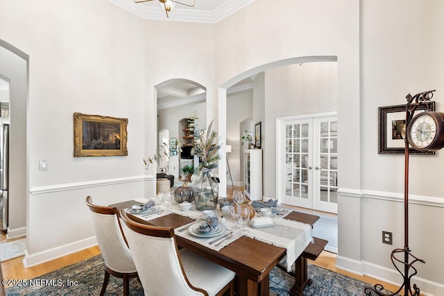 dining space featuring a towering ceiling, wood-type flooring, ornamental molding, and french doors